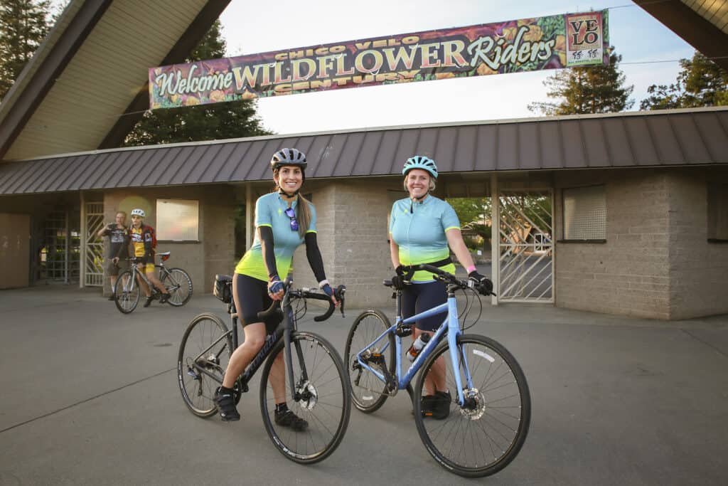 Two female riders smiling at the camera at the starting point of the Chico Velo Wildflower Century