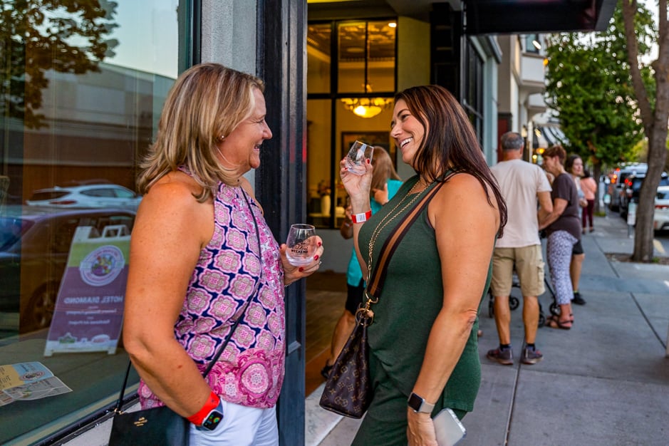 Two women laughing and smiling while drinking wine outside of the Hotel Diamond during the Downtown Chico Art and Wine Walk