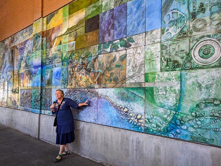 A tour guide stands in front of a large mosaic mural during the Downtown Chico Public Art Tours
