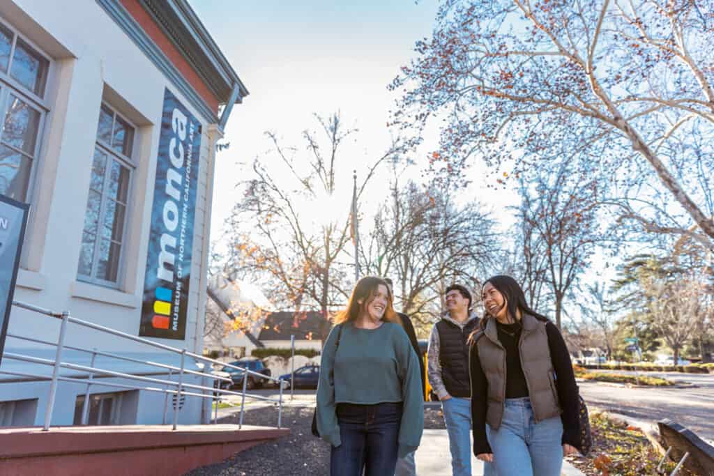 Two young women smiling at each as they walk outside of the Museum of Northern California Art in the winter