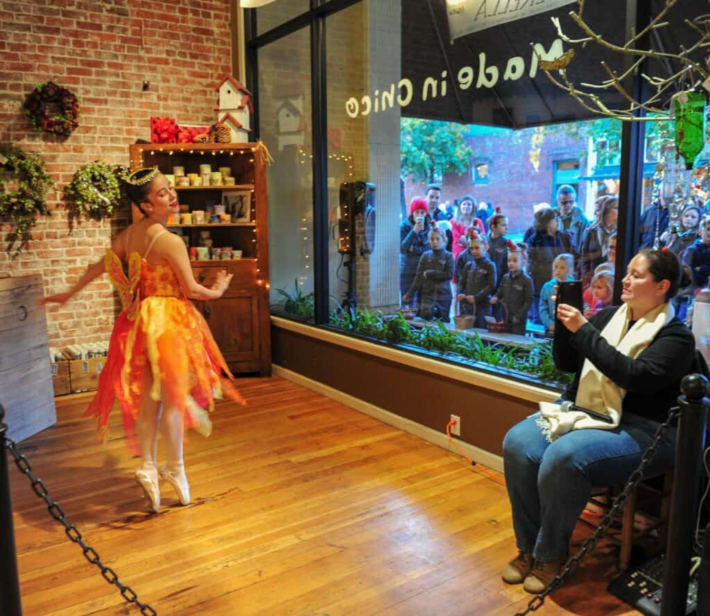 A young ballerina dances in a store window and people are watching from the outside during Chico's Christmas Preview