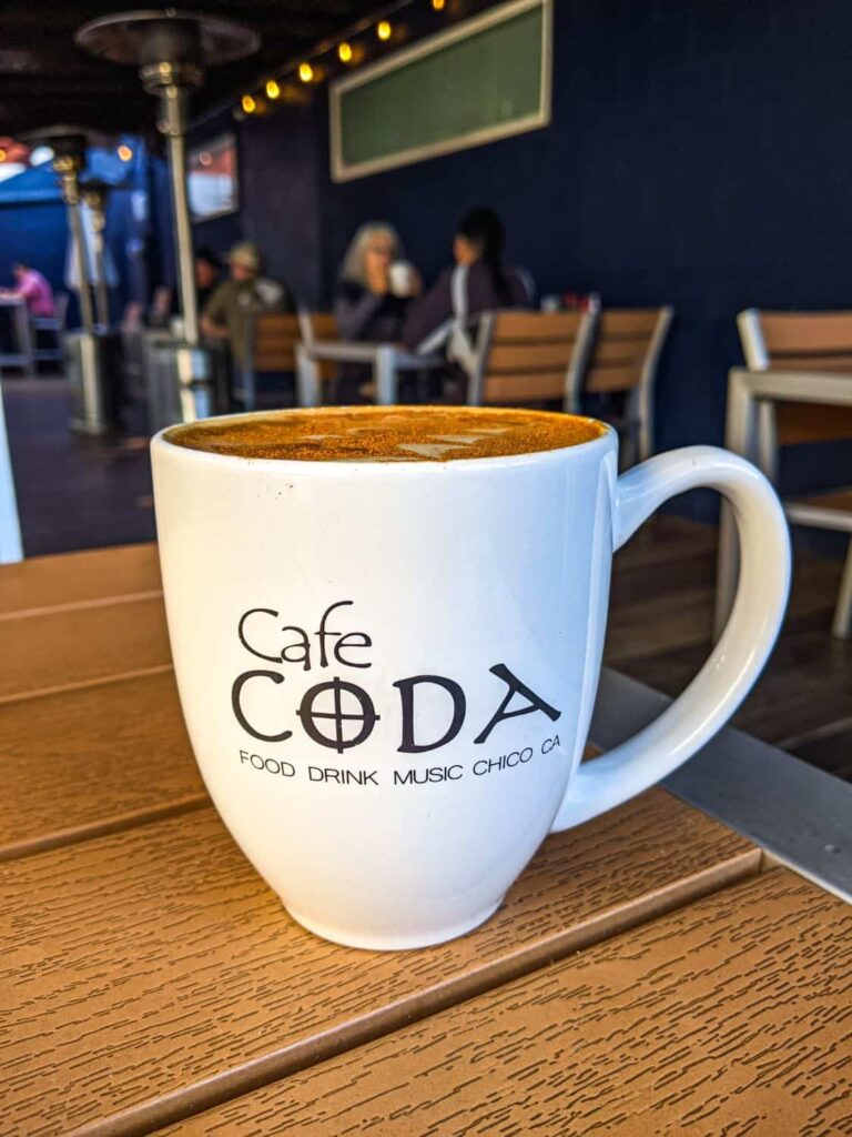 Close-up of a white coffee mug filled with a latte. The mug has Cafe Coda written on it