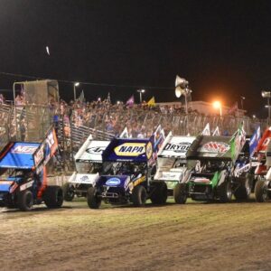 A row of stock cars racing on the dirt track at Silver Dollar Fairgrounds during the Gold Cup Race of Champions