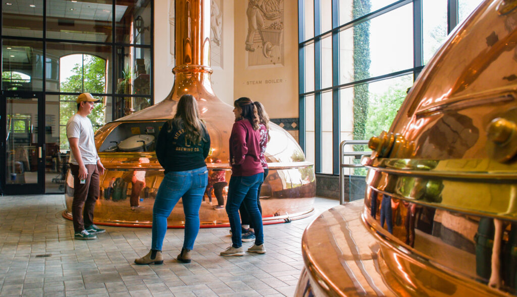 Three people stand near two copper brewing stills at Sierra Nevada Brewing Company in Chico