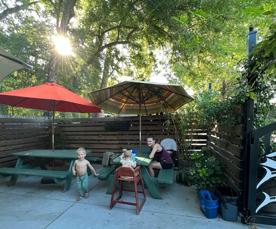 A mom with two kids sitting under umbrellas in a shaded patio at a coffee chop