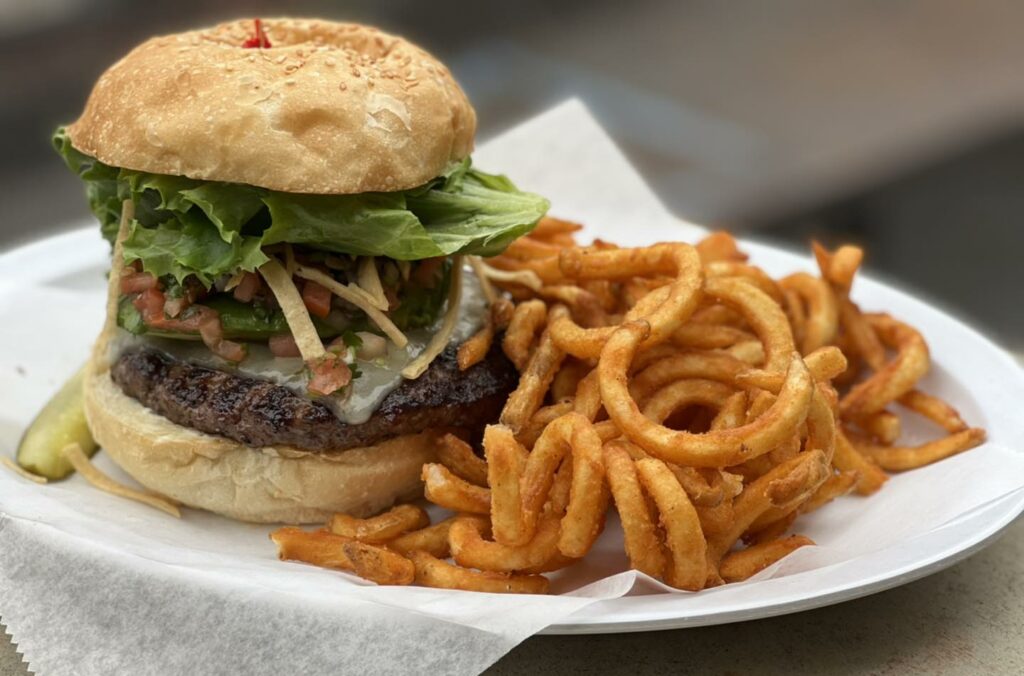 A loaded hamburger on a plate with curly fries at Burgers & Brew