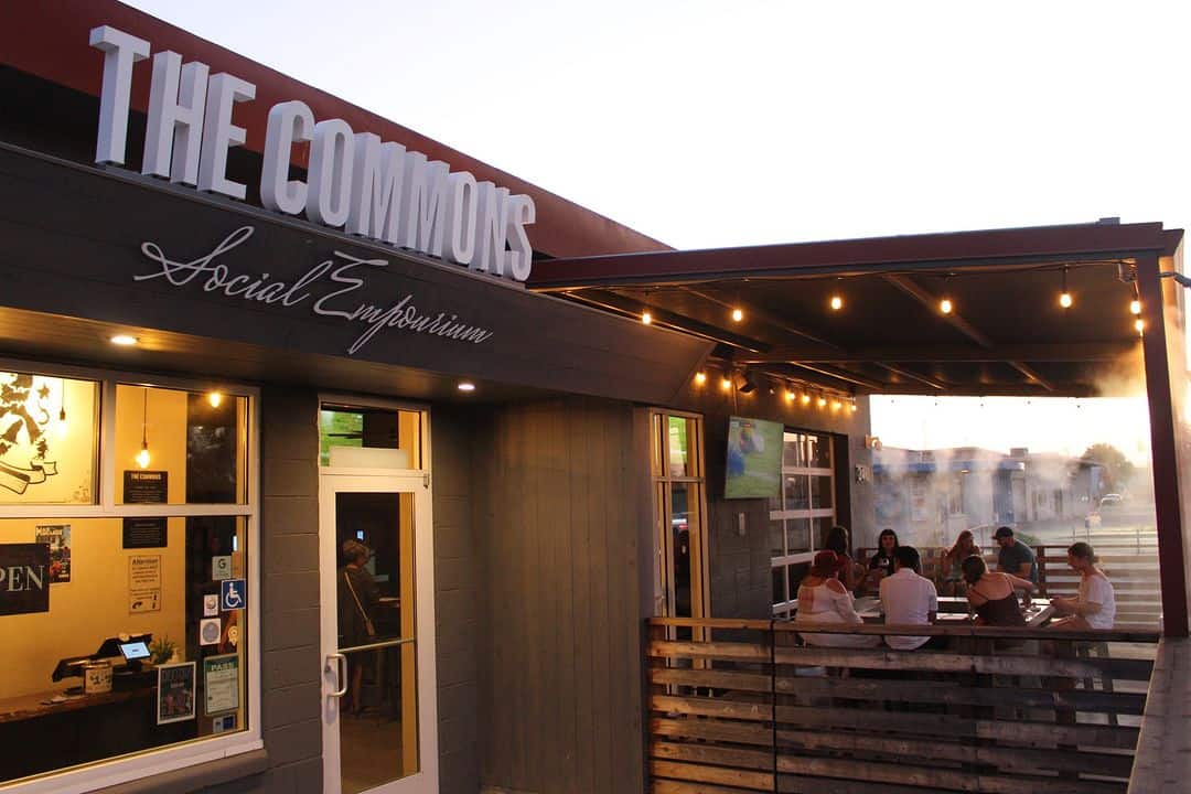 Outside of The Commons at dusk, with people sitting on a patio that has misters on and bar lights