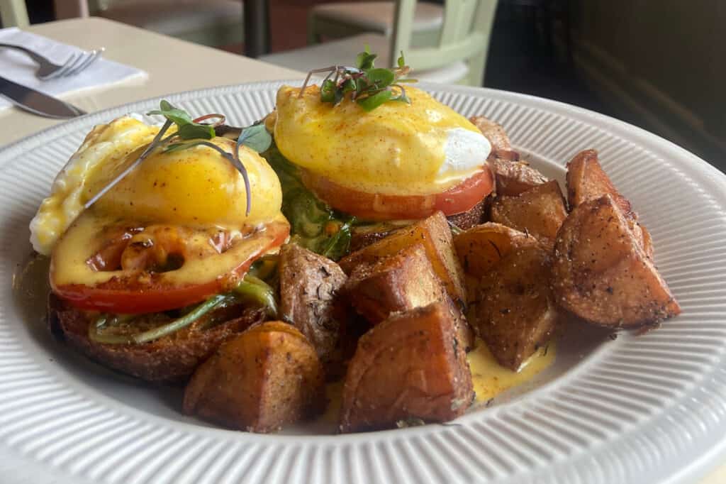 Close-up of eggs benedict with home fries on a white plate at Deja Vu Breakfast Company