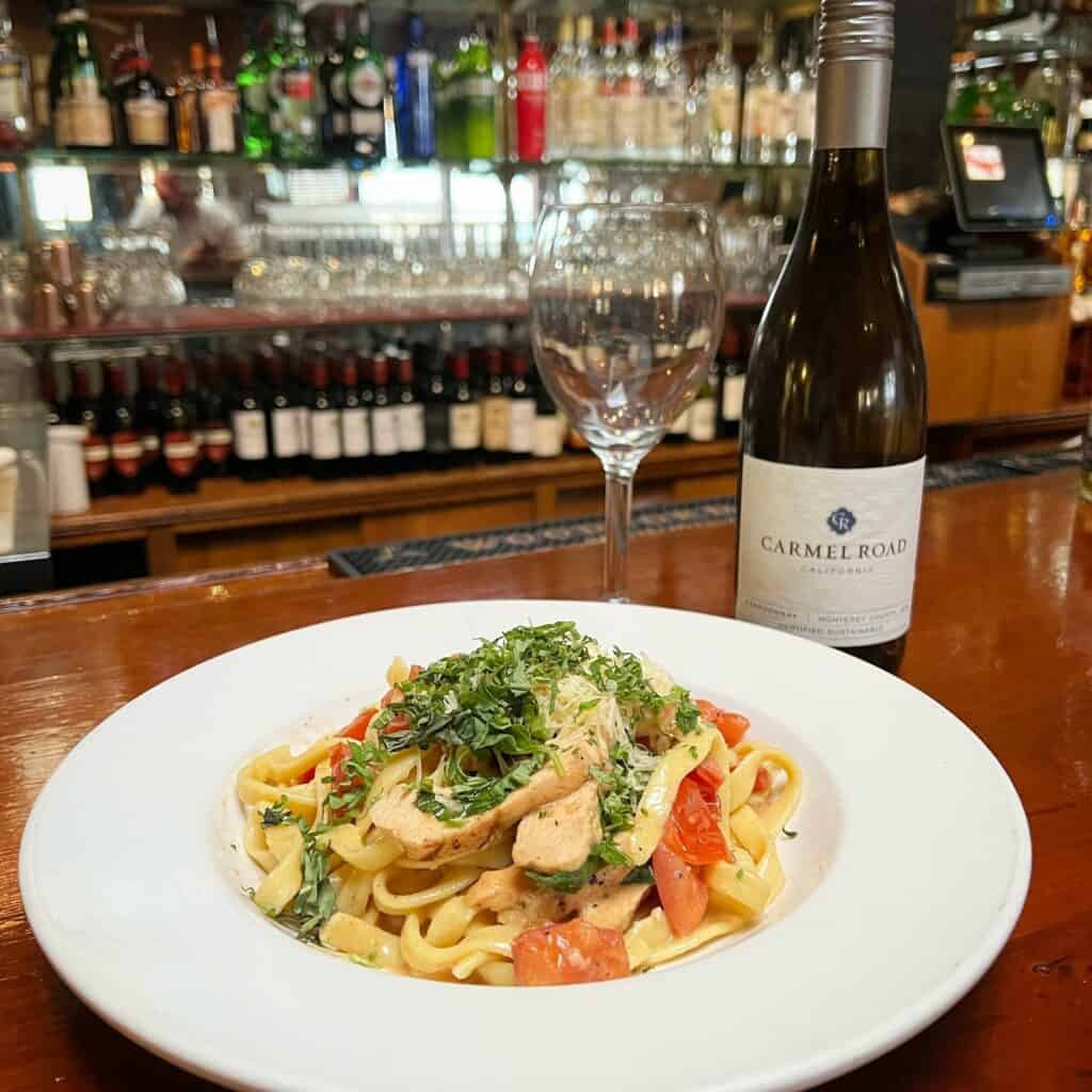 A bowl of pasta with a bottle of wine on the bar at Franky's