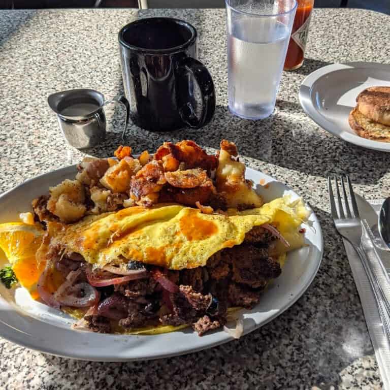 A plate with a meat-filled omelet and home fries with a English muffin on the side