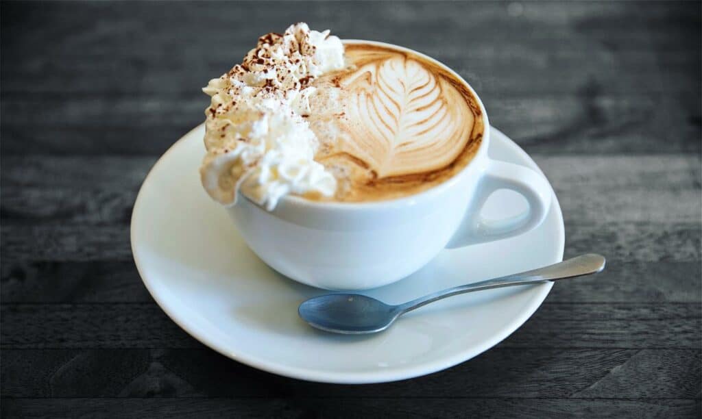 Close-up of a latte with latte art and whipped cream in a white cup and saucer from Naked Lounge