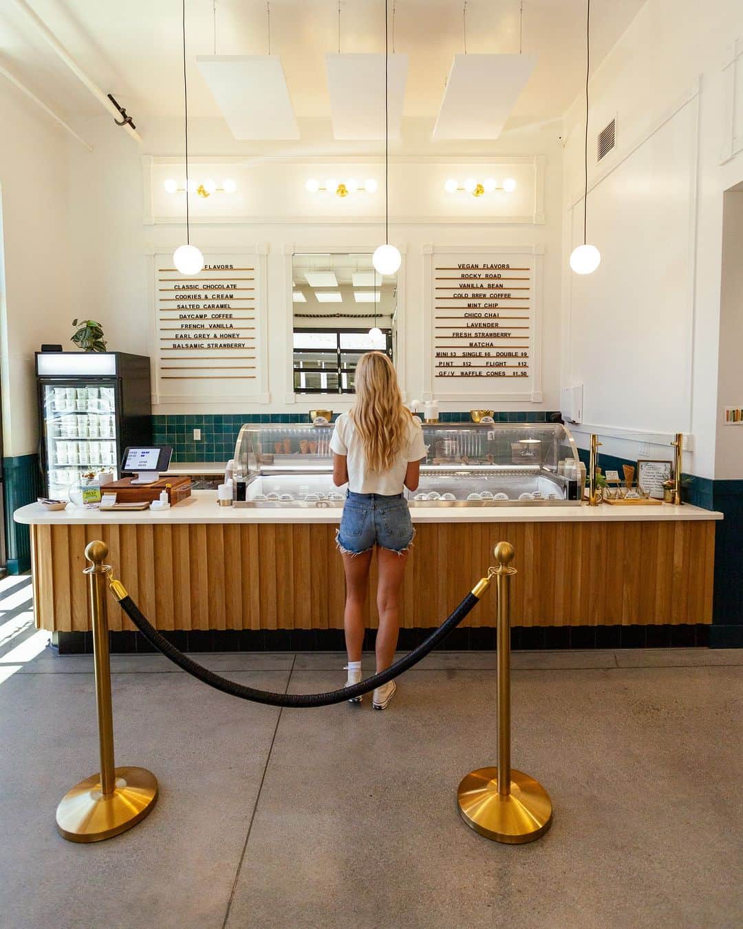 A woman standing at the ordering counter in an ice cream shop, looking at the menu and ice cream varieties