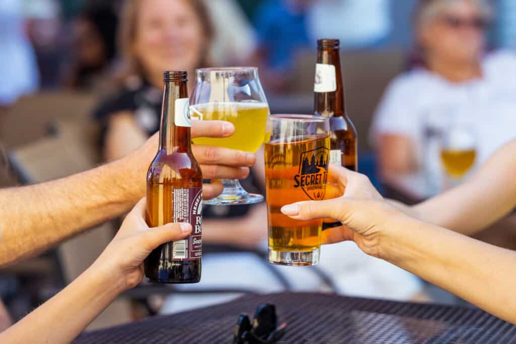 Four hands coming together to cheers beer pints and root beer glasses at Secret Trail Brewing Company