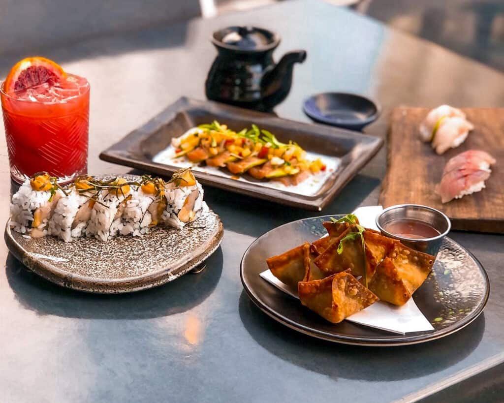 Three plates of sushi rolls and appetizers with drinks at the Rawbar Restaurant & Sushi