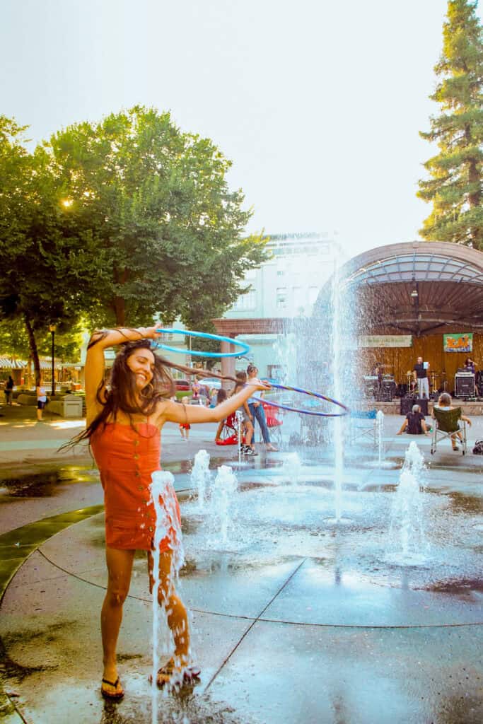 A woman dancing with a hula hoop in front of water fountains