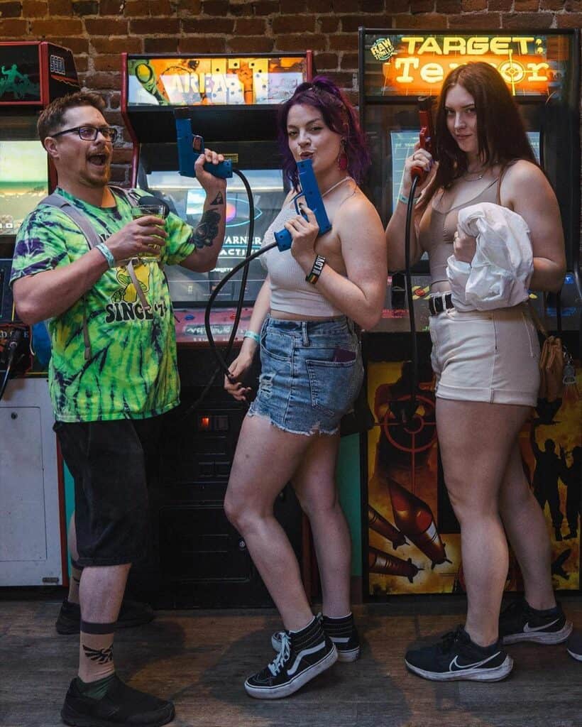 Three friends posing with video game target guns at Coin-Op Game Room in Chico
