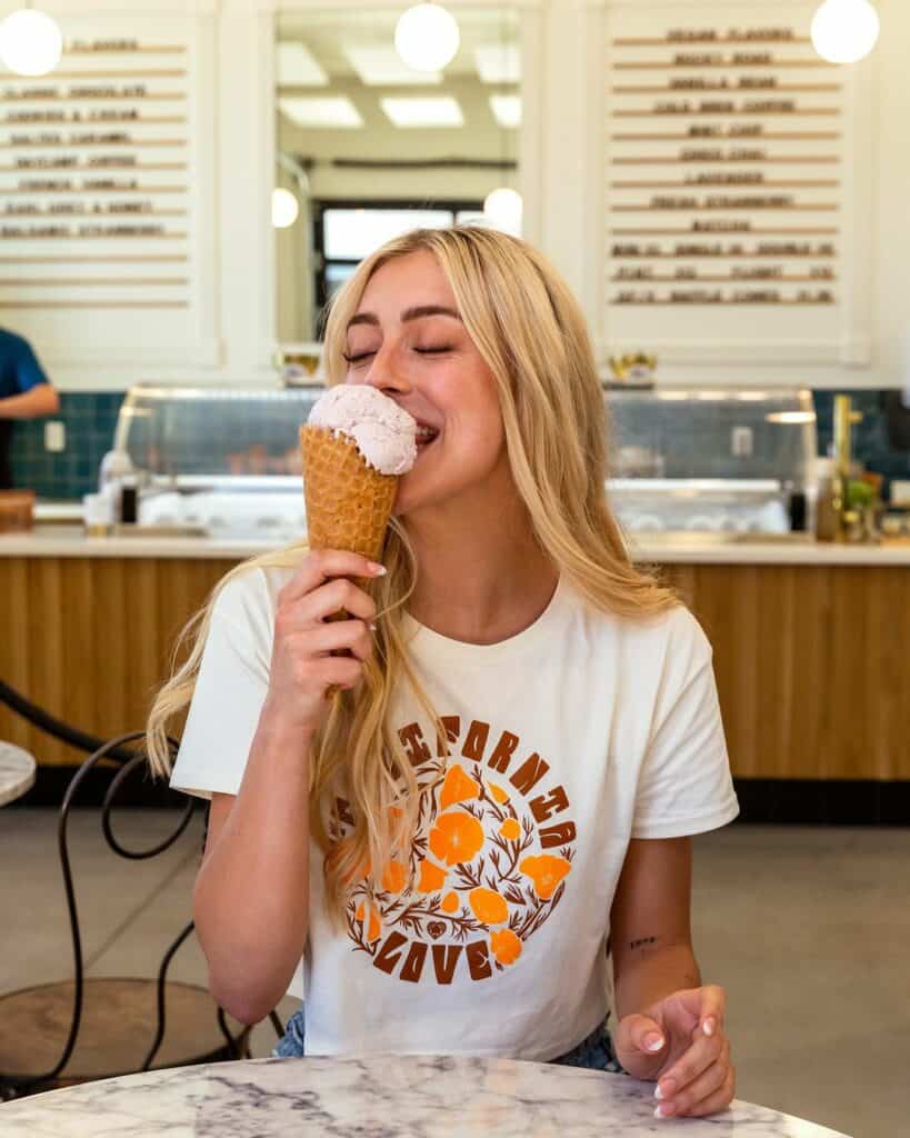 A woman smiling as she bites into an ice cream cone