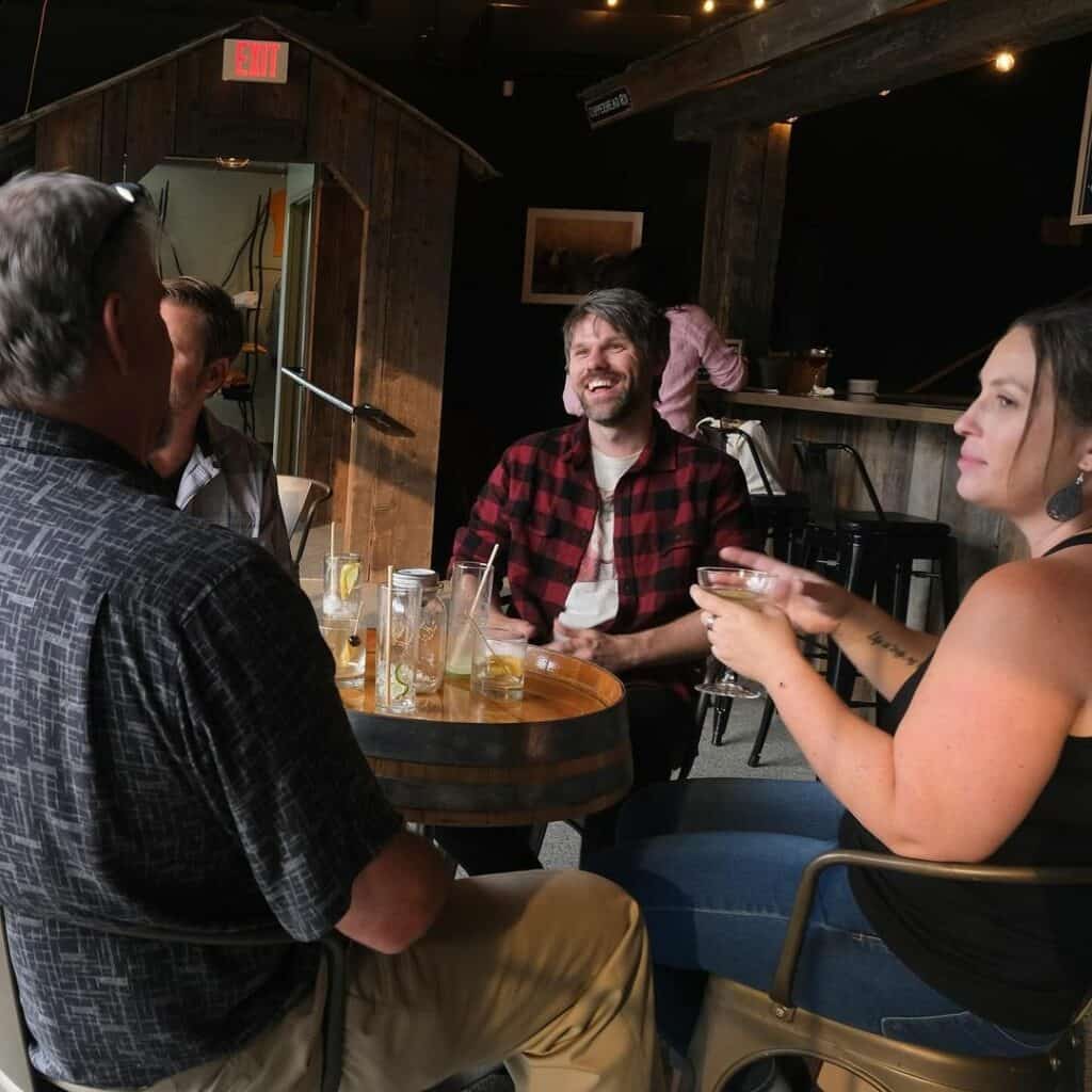 People sitting around a barrel table sampling liquor