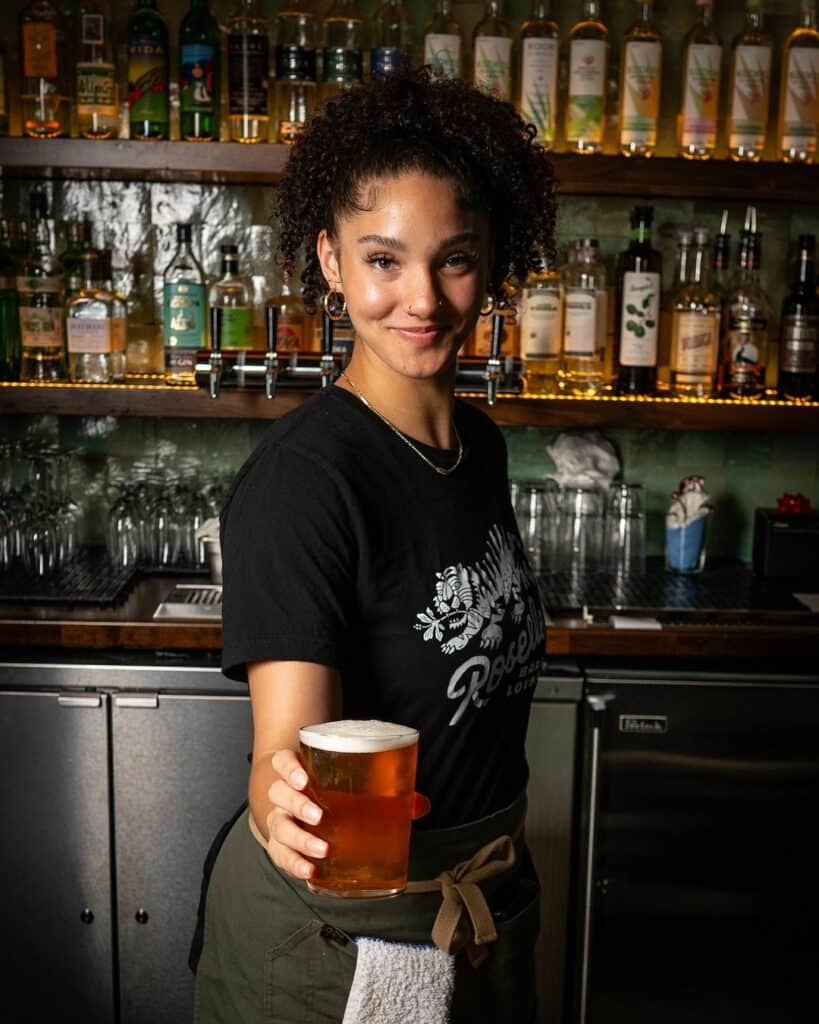 A woman holds out a glass of beer while staring into the camera
