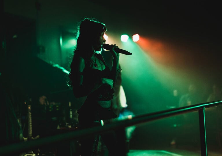 A backlit burlesque dancer speaking into a microphone.